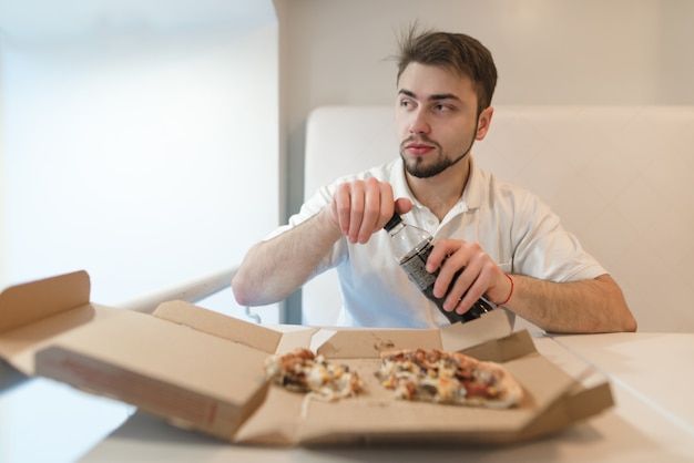 Um homem abre uma garrafa com uma bebida no fundo da pizza. Um homem bebe uma pizza com uma cola.