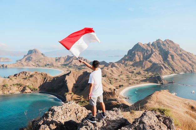 Um homem acenando uma bandeira da Indonésia no topo das colinas da ilha padar labuan bajo