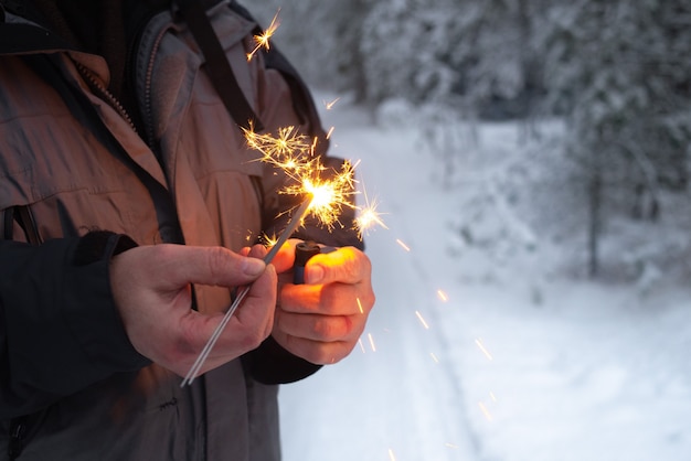 Um homem acende estrelinhas em uma floresta de inverno.