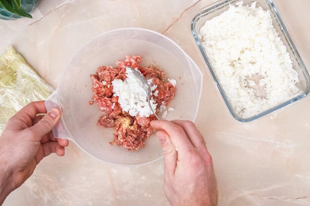 Um homem adiciona arroz cozido à carne picada para os rolos de repolho preguiçosos na mesa