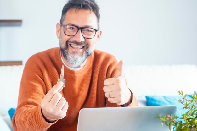 Um homem adulto alegre mostrando o novo hone ket e o polegar para cima sorrindo para a câmera Encontrar casa apartamento on-line em conceito de site Pesquisa de propriedade na web Negócios imobiliários pessoas e caderno