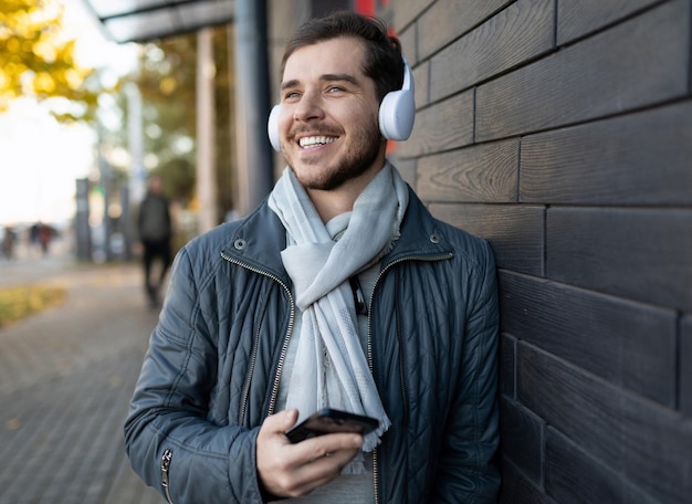 Um homem adulto alegre ouve música em fones de ouvido brancos em um telefone celular e olha para