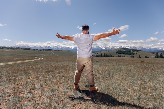 Um homem adulto brutal fica de costas para uma clareira verde, abrindo os braços e olhando para uma vista de floresta de verão com montanhas zhiaopis. o conceito de liberdade.