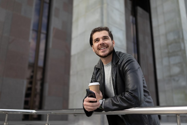 Um homem adulto com um sorriso fica com uma xícara de café e um telefone celular e olha para cima