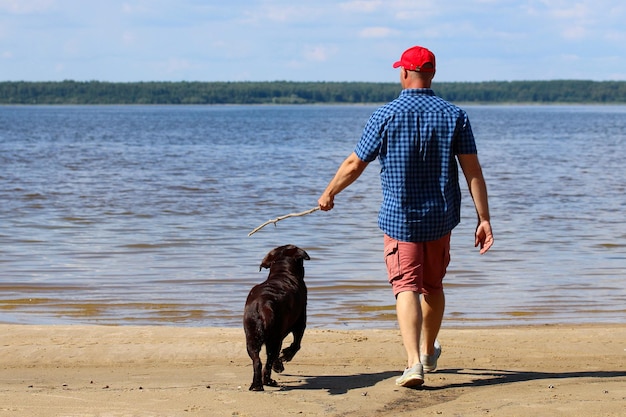 Um homem adulto está brincando com um cachorro, o dono está andando com um animal de estimação na margem do rio