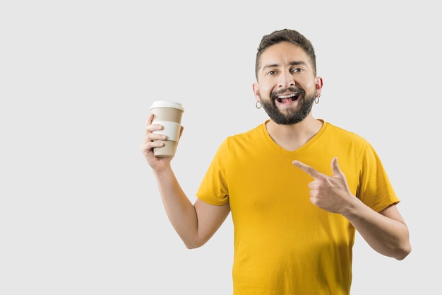 Um homem adulto latino com camisa amarela sobre fundo branco está apontando para uma xícara de café