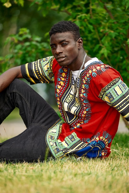 Um homem africano com roupas nacionais da áfrica do sul, um jovem negro descansando em um parque com roupas nacionais.