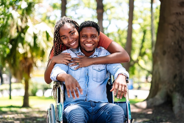 Um homem afro-americano em uma cadeira de rodas, desfrutando de um passeio no parque com a namorada.