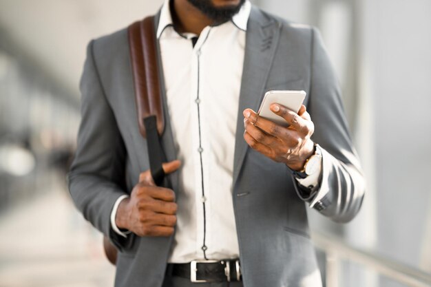 Um homem afro-americano está usando seu telefone em um terminal de aeroporto de pé com sua bagagem