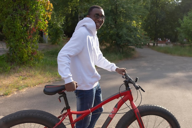 Um homem afro-americano sorridente feliz com uma bicicleta em um parque público Esportes e recreação