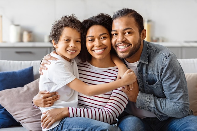 Um homem afro-americano, uma mulher e uma criança estão sentados juntos num sofá. Parecem relaxados e...