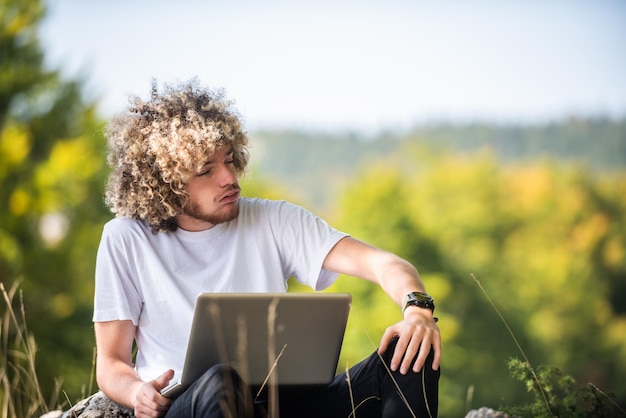 Um homem afro sentado na natureza e usando um laptop para uma reunião online durante uma pandemia de coronavírus