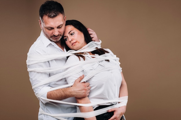 Um homem agressivo abraça uma mulher agredida e é envolvido por bandagens. Violência doméstica