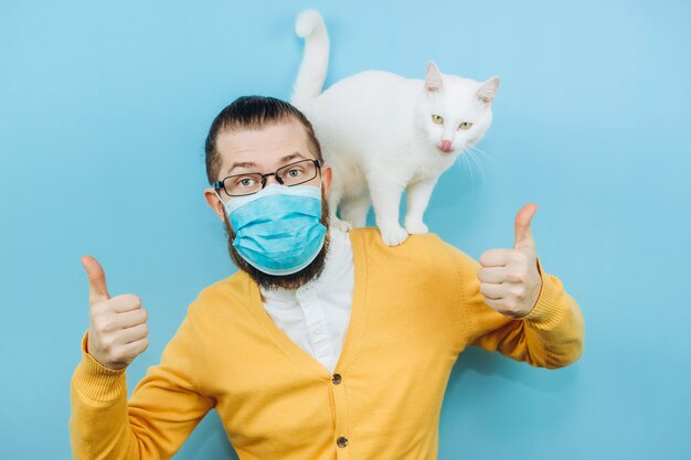 Um homem alegre em uma máscara médica com um gato branco no ombro. Pandemia COVID 2019. Pet.