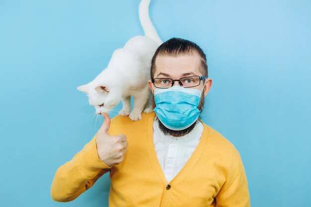 Um homem alegre em uma máscara médica com um gato branco no ombro. Pandemia COVID 2019. Pet.