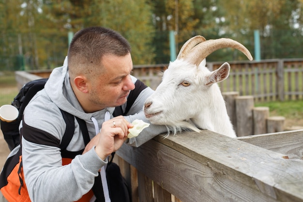 Um homem alimentando uma maçã para uma cabra no zoológico