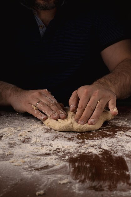 Um homem amassa faz massa em um fundo escuro Preparação de massa de pizza