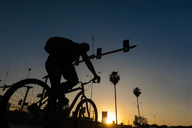 Um homem anda de bicicleta em uma cidade ao pôr do sol sobre o fundo das palmas das silhuetas