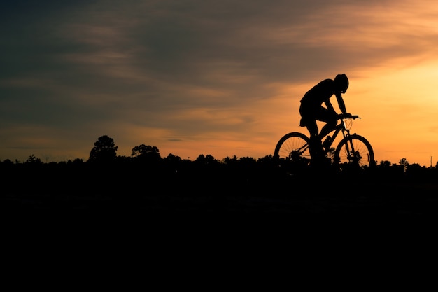 Um homem anda de bicicleta na estrada no fundo do céu por do sol.