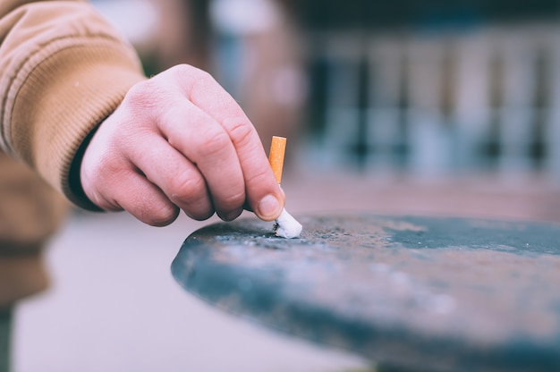 Foto um homem apaga um cigarro no lixo.