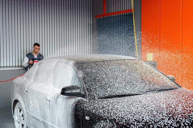 Um homem aplica espuma a um carro para remover a sujeira em uma lavagem de carros