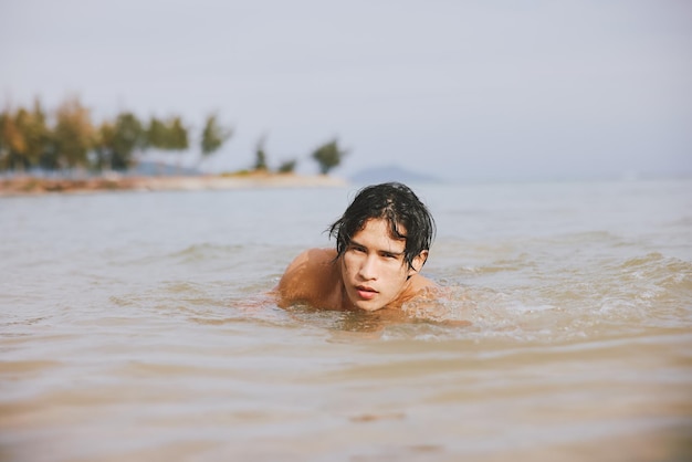 Um homem asiático a desfrutar de férias na praia tropical no oceano azul.