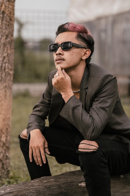 Um homem asiático com óculos escuros e um blazer cinza está apreciando a vista no parque