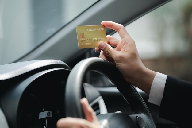 Um homem asiático em um terno formal está em um carro ele segura um cartão de crédito ele dirige em um posto de gasolina e paga suas contas de cartão de crédito viagem de carro condução segura respeitando as regras de trânsito