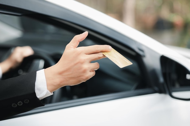 Um homem asiático em um terno formal fica no carro abre a janela entregou seu cartão de crédito para pagar a viagem de gás de carro dirigindo com segurança respeitando as regras de trânsito