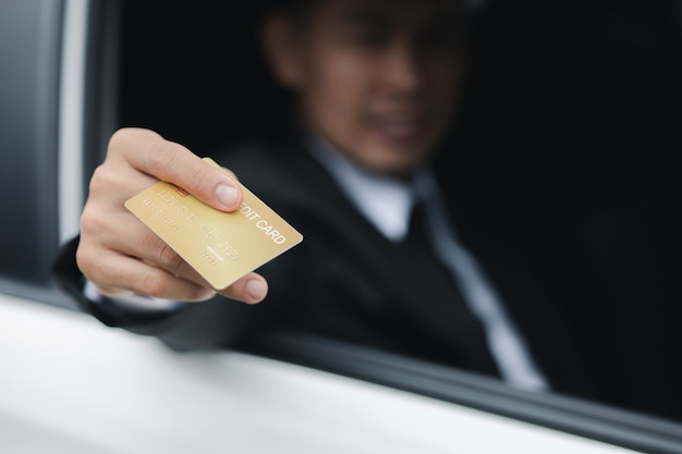 Um homem asiático em um terno formal fica no carro abre a janela entregou seu cartão de crédito para pagar a viagem de gás de carro dirigindo com segurança respeitando as regras de trânsito