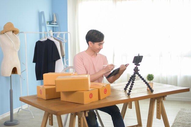 Um homem asiático está mostrando roupas na frente do smartphone transmitindo ao vivo em sua loja