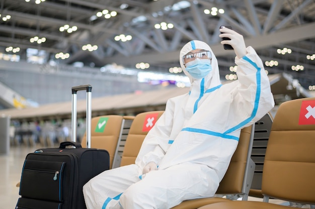 Um homem asiático está usando um traje de proteção pessoal no aeroporto internacional, viagens seguras, proteção covid-19, conceito de distanciamento social