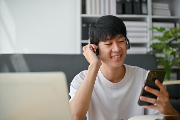 Um homem asiático feliz usando fones de ouvido escolhendo listas de reprodução de música em seu telefone