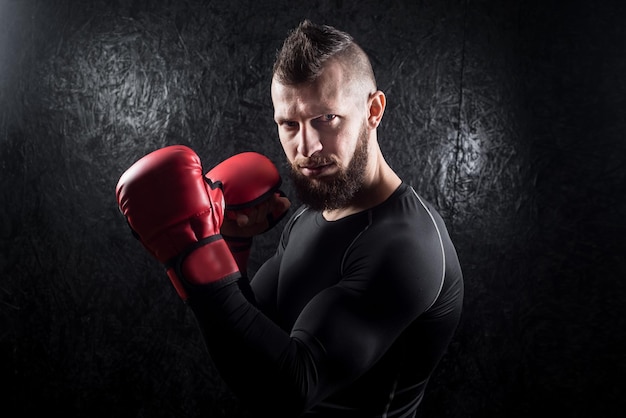 Um homem atlético usando luvas de kickboxing vermelhas posando e pronto para lutar no ginásio