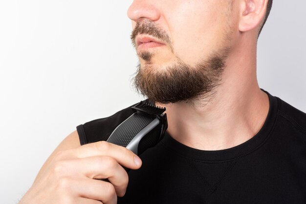 Foto um homem barbudo apara a barba com um aparador em um plano de fundo claro