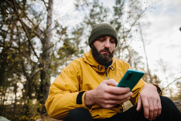 Um homem barbudo descansa em uma árvore caída no meio da floresta Um homem usa um telefone celular para pesquisar GPS