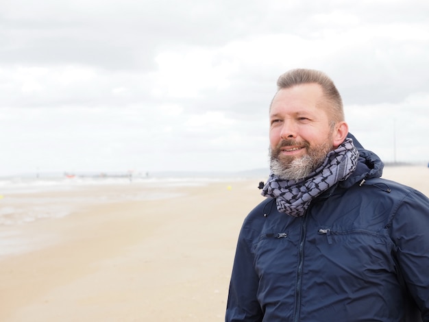 Um homem barbudo em pé na praia no oceano Um vento forte está soprando