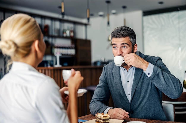 Um homem barbudo está tomando seu café enquanto está sentado com sua namorada em uma cafeteria