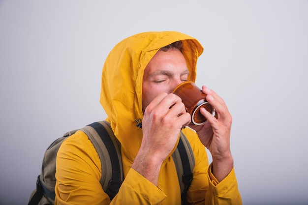 Um homem bebe chá de ervas saudável enquanto veste uma capa de chuva