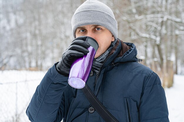 Um homem bebe de um termo roxo em uma caminhada de inverno