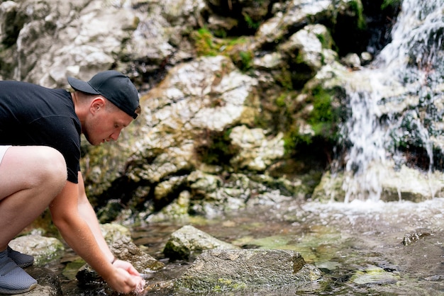 Um homem bebendo água pura do rio da montanha