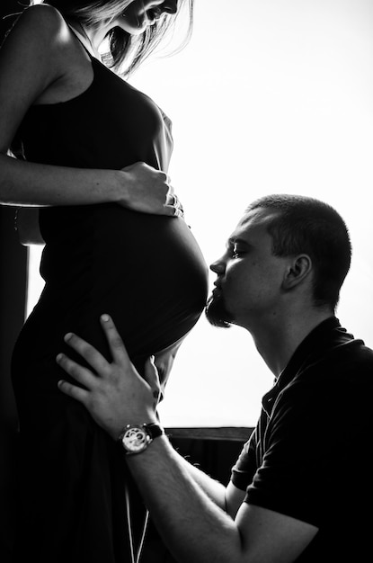 Um homem beija sua esposa grávida no estômago Foto em preto e branco