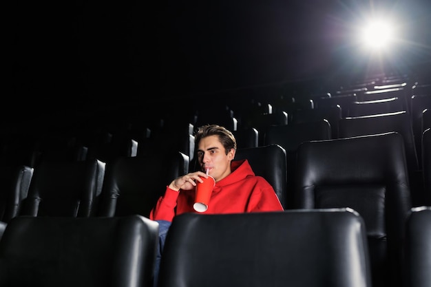 Foto um homem bonito bebe refrigerante de um copo de papel enquanto assiste a um filme no cinema