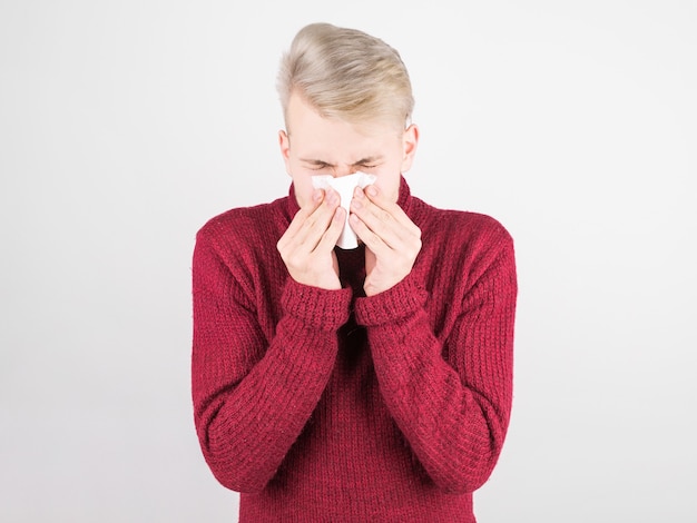 Um homem bonito com um lenço vermelho está resfriado e assoa o nariz em um guardanapo. O conceito de medicina e resfriados sazonais.