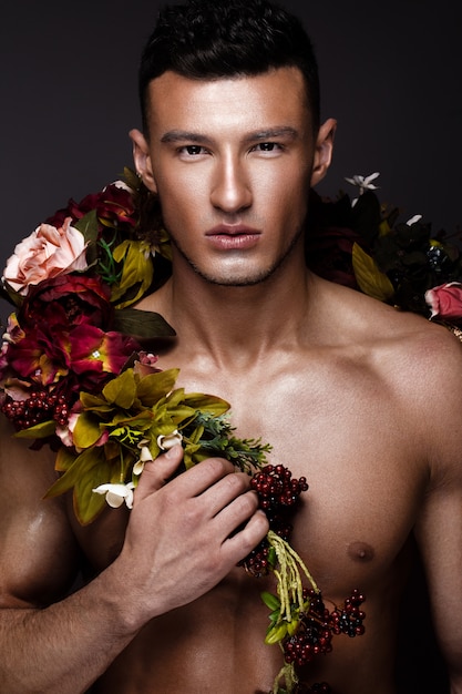 Um homem bonito, com um torso nu, bronzeado e flores no corpo.