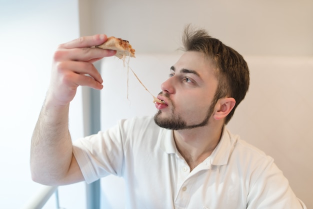 Um homem bonito come um pedaço quente de pizza. o homem come um queijo que se estende com uma fatia de pizza.