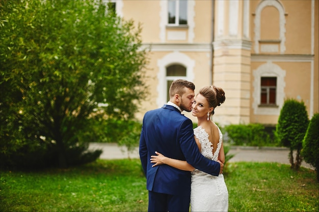 Um homem bonito em um moderno terno azul abraçando e beijando uma linda modelo mulher em um vestido de noiva