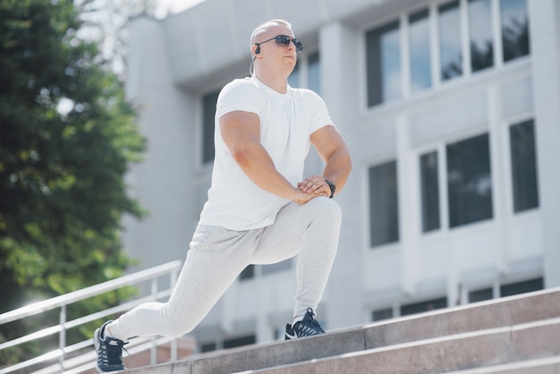 Um homem bonito fitness em um sportswear, fazendo alongamentos enquanto se prepara para exercícios sérios na cidade moderna