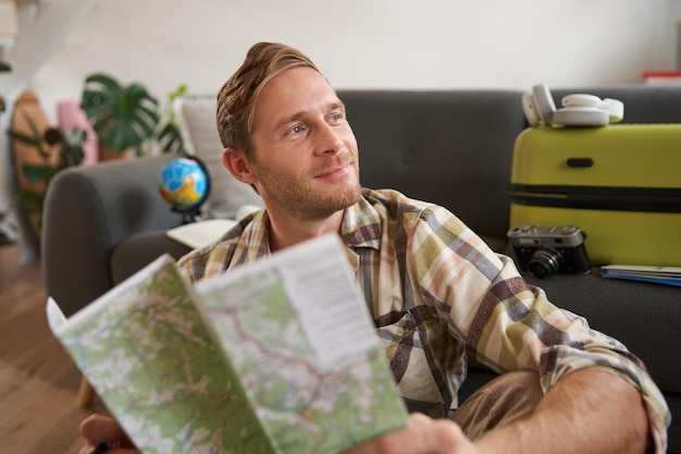 Um homem bonito sorridente com um mapa nas mãos, uma mala embalada, vai de férias, preparado para ir de férias.