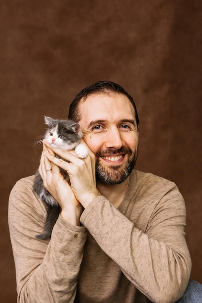 Foto um homem brinca com um gatinho, abraça-o e beija-o.